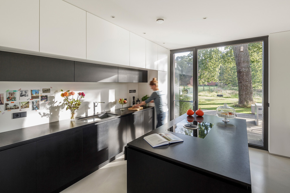 Modern galley kitchen in Other with an undermount sink, flat-panel cabinets, black cabinets, concrete floors, with island, grey floor and black benchtop.