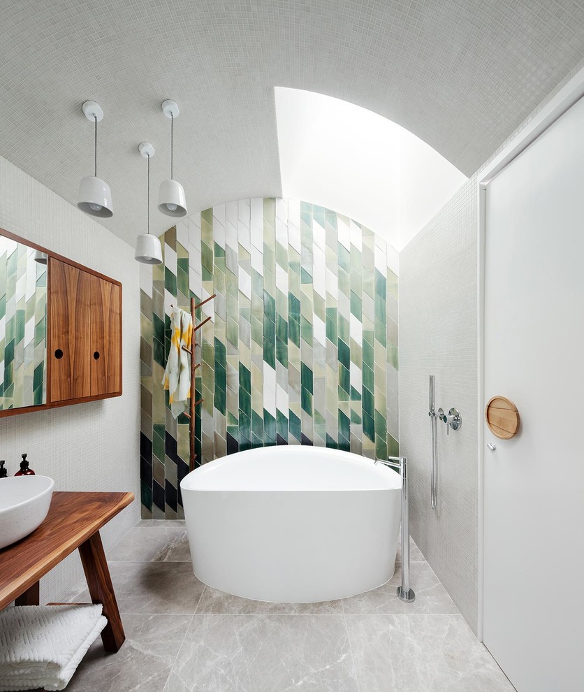 Mid-sized contemporary master bathroom in Sydney with medium wood cabinets, a freestanding tub, a wall-mount toilet, green tile, ceramic tile, white walls, marble floors, a vessel sink, wood benchtops and brown benchtops.