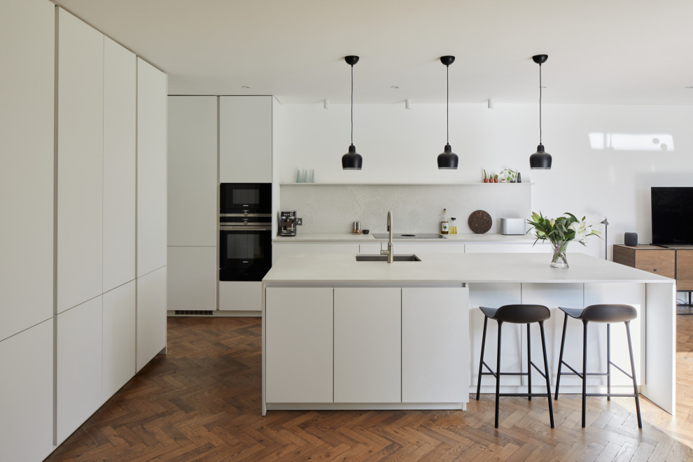 Photo of a medium sized modern l-shaped open plan kitchen in London with flat-panel cabinets, white cabinets, engineered stone countertops, grey splashback, an island and grey worktops.