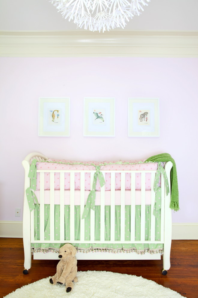 This is an example of a traditional nursery for girls in Atlanta with pink walls and medium hardwood floors.