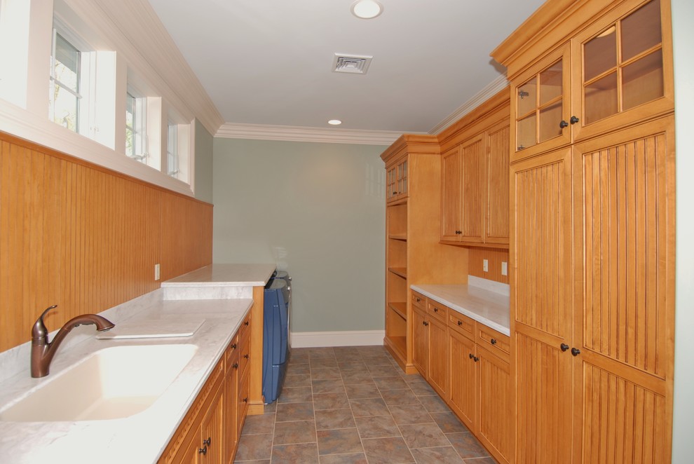 Photo of an expansive traditional galley dedicated laundry room in New York with light wood cabinets, solid surface benchtops, green walls, porcelain floors, a side-by-side washer and dryer, beaded inset cabinets, grey floor and an undermount sink.