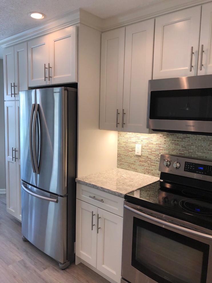 This is an example of a mid-sized beach style l-shaped separate kitchen in New York with an undermount sink, shaker cabinets, white cabinets, quartzite benchtops, blue splashback, glass tile splashback, stainless steel appliances, laminate floors, no island, grey floor and green benchtop.