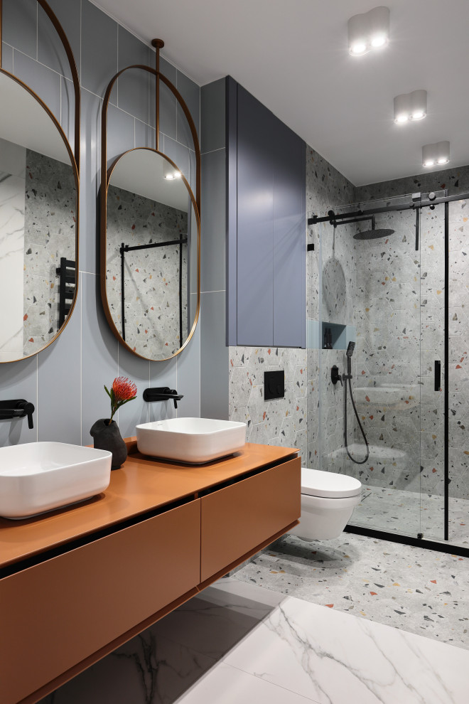 Mid-sized contemporary bathroom in Saint Petersburg with flat-panel cabinets, orange cabinets, an alcove shower, a wall-mount toilet, blue tile, ceramic tile, multi-coloured walls, porcelain floors, solid surface benchtops, multi-coloured floor, a sliding shower screen, orange benchtops, a double vanity, a floating vanity and a vessel sink.