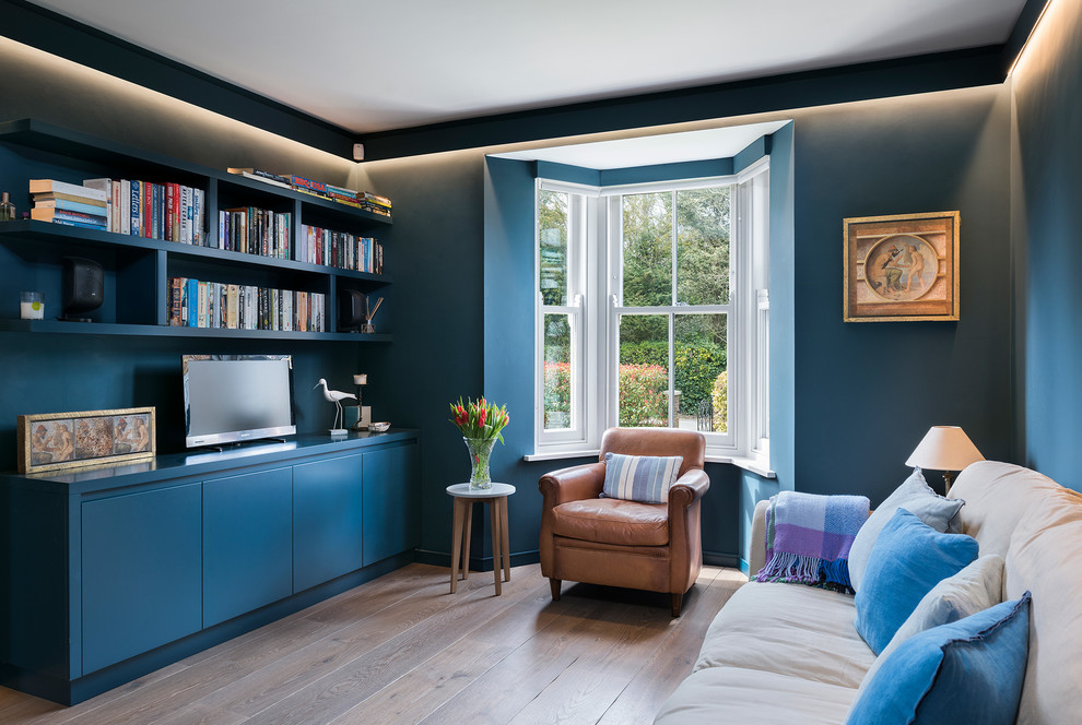 This is an example of a transitional family room in Hampshire with a library, blue walls, medium hardwood floors and a freestanding tv.