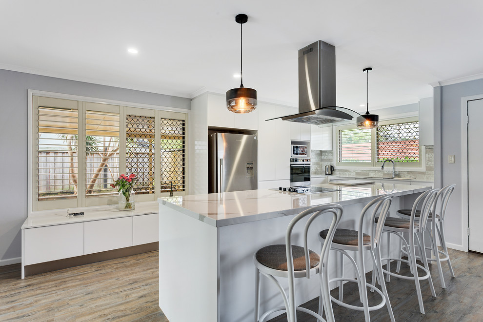 Inspiration for a mid-sized transitional eat-in kitchen in Gold Coast - Tweed with an undermount sink, flat-panel cabinets, white cabinets, quartz benchtops, grey splashback, ceramic splashback, stainless steel appliances, with island and white benchtop.