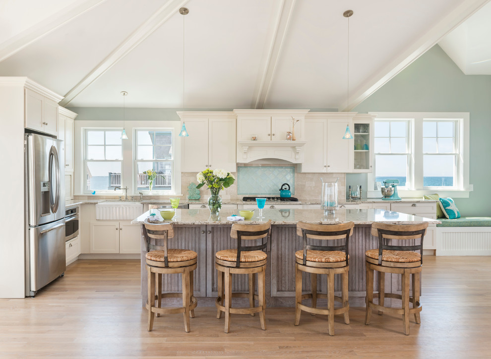Large beach style l-shaped kitchen in Providence with a farmhouse sink, white cabinets, granite benchtops, blue splashback, stainless steel appliances, light hardwood floors, with island, shaker cabinets and glass tile splashback.
