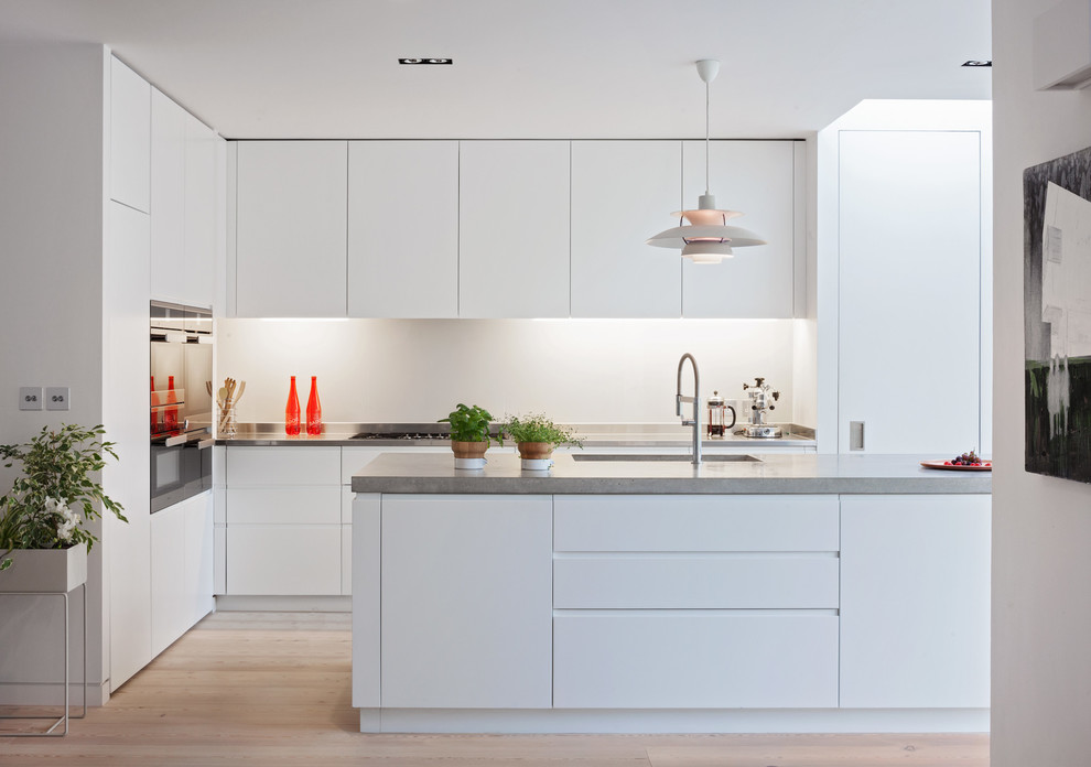Design ideas for a mid-sized contemporary single-wall eat-in kitchen in London with an integrated sink, flat-panel cabinets, white cabinets, concrete benchtops, white splashback, glass sheet splashback, panelled appliances, painted wood floors and with island.