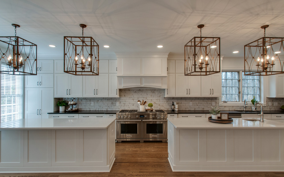 Inspiration for a large cottage medium tone wood floor and brown floor eat-in kitchen remodel in Nashville with an undermount sink, shaker cabinets, white cabinets, quartz countertops, multicolored backsplash, porcelain backsplash, stainless steel appliances, two islands and white countertops