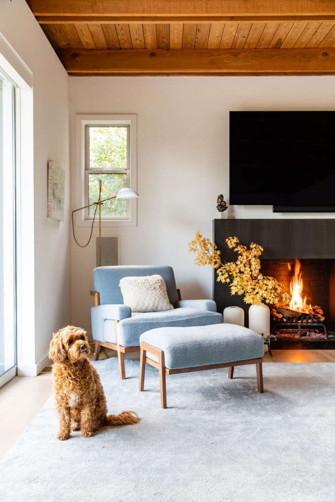 This is an example of a medium sized coastal open plan living room in San Francisco with white walls, a standard fireplace, a stone fireplace surround, a wall mounted tv, beige floors and a wood ceiling.
