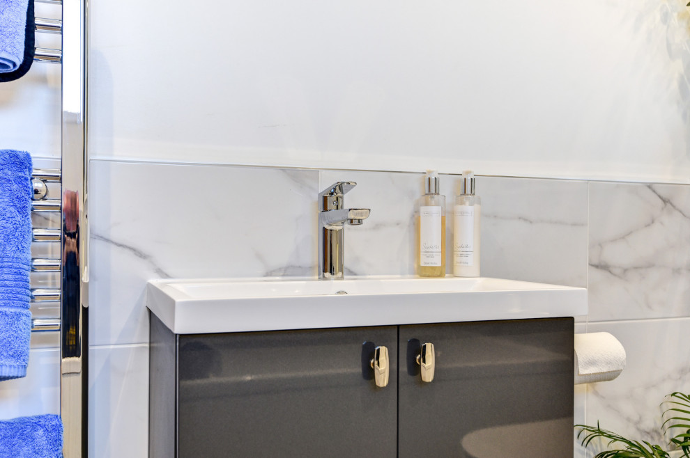 Small minimalist kids' white tile and marble tile laminate floor, brown floor and single-sink bathroom photo in Sussex with flat-panel cabinets, gray cabinets, a wall-mount toilet, white walls, an integrated sink, marble countertops, a niche and a built-in vanity