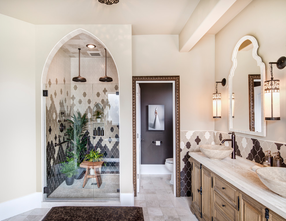 Mediterranean master bathroom in Seattle with light wood cabinets, a freestanding tub, ceramic tile, beige walls, ceramic floors, a vessel sink, marble benchtops, a hinged shower door, an alcove shower, beige tile, gray tile, white tile, beige floor, an enclosed toilet and raised-panel cabinets.