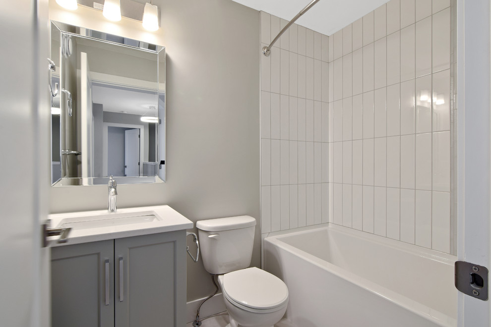 This is an example of a small arts and crafts bathroom in Other with shaker cabinets, grey cabinets, an alcove tub, a shower/bathtub combo, a two-piece toilet, white tile, subway tile, white walls, an undermount sink, solid surface benchtops, a shower curtain and white benchtops.