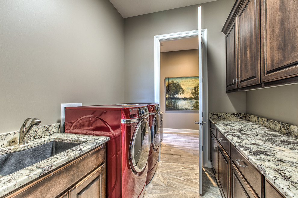 Inspiration for a mid-sized transitional galley dedicated laundry room in Omaha with an undermount sink, raised-panel cabinets, dark wood cabinets, granite benchtops, beige walls, porcelain floors, a side-by-side washer and dryer, brown floor and multi-coloured benchtop.