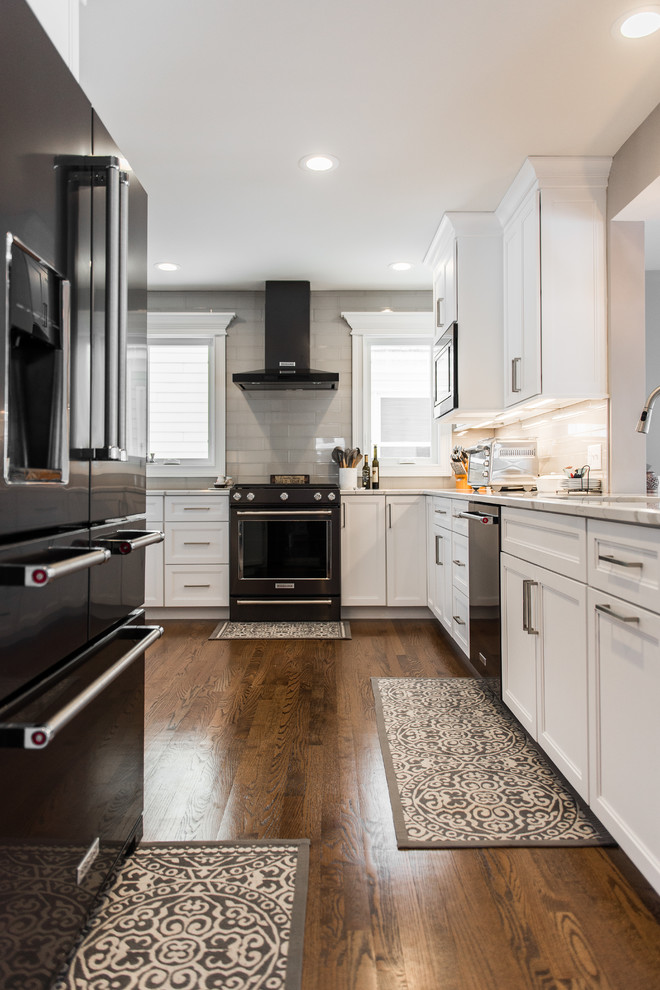 Inspiration for a mid-sized transitional l-shaped medium tone wood floor and brown floor eat-in kitchen remodel in Chicago with an undermount sink, recessed-panel cabinets, white cabinets, quartzite countertops, gray backsplash, subway tile backsplash, black appliances, no island and multicolored countertops