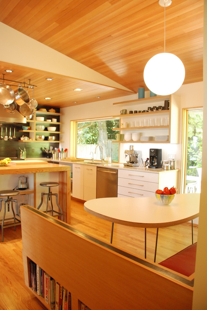 Photo of a modern kitchen in Portland with flat-panel cabinets, white cabinets, wood benchtops, an undermount sink, stainless steel appliances, light hardwood floors and with island.