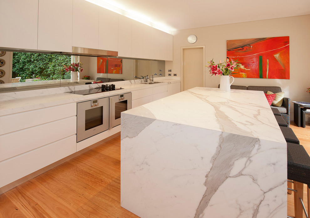 Design ideas for a large contemporary galley eat-in kitchen in Sydney with an undermount sink, flat-panel cabinets, white cabinets, marble benchtops, metallic splashback, glass sheet splashback, stainless steel appliances, medium hardwood floors and with island.