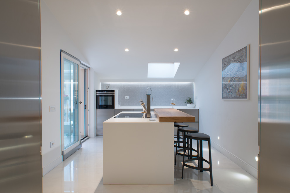 Mid-sized contemporary open plan kitchen in Naples with a single-bowl sink, flat-panel cabinets, stainless steel cabinets, grey splashback, with island, ceramic splashback, stainless steel appliances and porcelain floors.