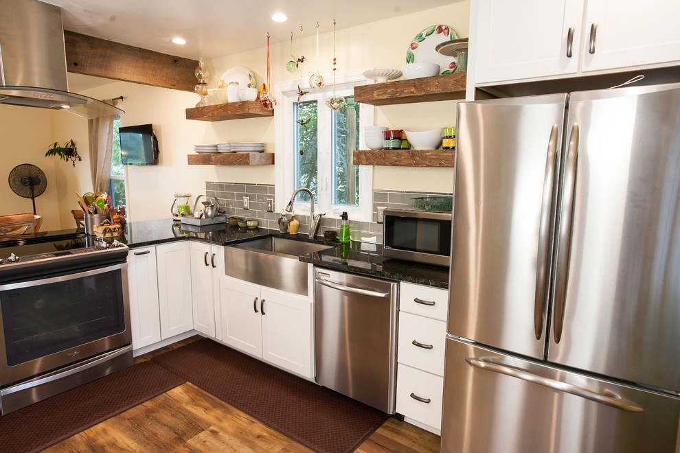 This is an example of a large arts and crafts l-shaped open plan kitchen in Baltimore with a farmhouse sink, shaker cabinets, white cabinets, granite benchtops, grey splashback, subway tile splashback, stainless steel appliances, vinyl floors and a peninsula.