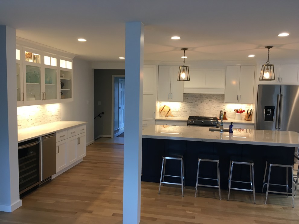 Example of a mid-sized transitional u-shaped brown floor open concept kitchen design in DC Metro with an undermount sink, shaker cabinets, white cabinets, gray backsplash, stainless steel appliances, an island and white countertops