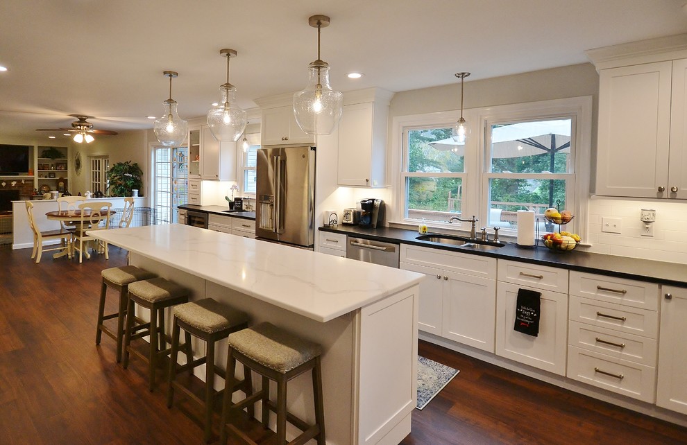 Photo of an expansive transitional u-shaped eat-in kitchen in Philadelphia with an undermount sink, recessed-panel cabinets, white cabinets, quartz benchtops, white splashback, subway tile splashback, stainless steel appliances, vinyl floors, with island, brown floor and white benchtop.