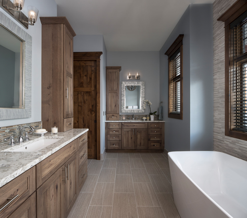 Mountain style multicolored tile and ceramic tile ceramic tile and beige floor freestanding bathtub photo with recessed-panel cabinets, brown cabinets, blue walls, an undermount sink and quartz countertops