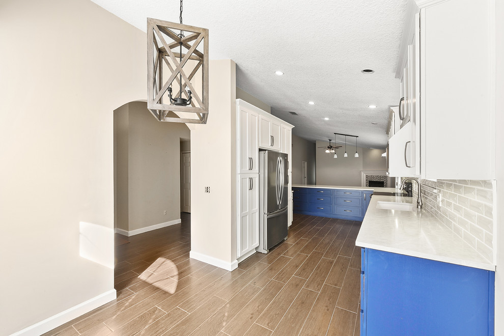 Open concept kitchen - large transitional l-shaped vinyl floor and brown floor open concept kitchen idea in Jacksonville with an undermount sink, shaker cabinets, blue cabinets, quartzite countertops, white backsplash, ceramic backsplash, stainless steel appliances and a peninsula