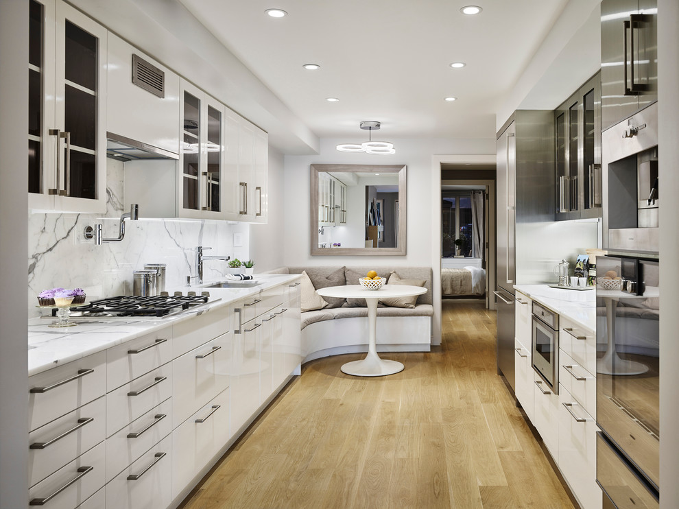 Photo of a large modern single-wall separate kitchen in New York with a single-bowl sink, raised-panel cabinets, white cabinets, stainless steel benchtops, white splashback, stone slab splashback, stainless steel appliances, light hardwood floors, multiple islands and brown floor.