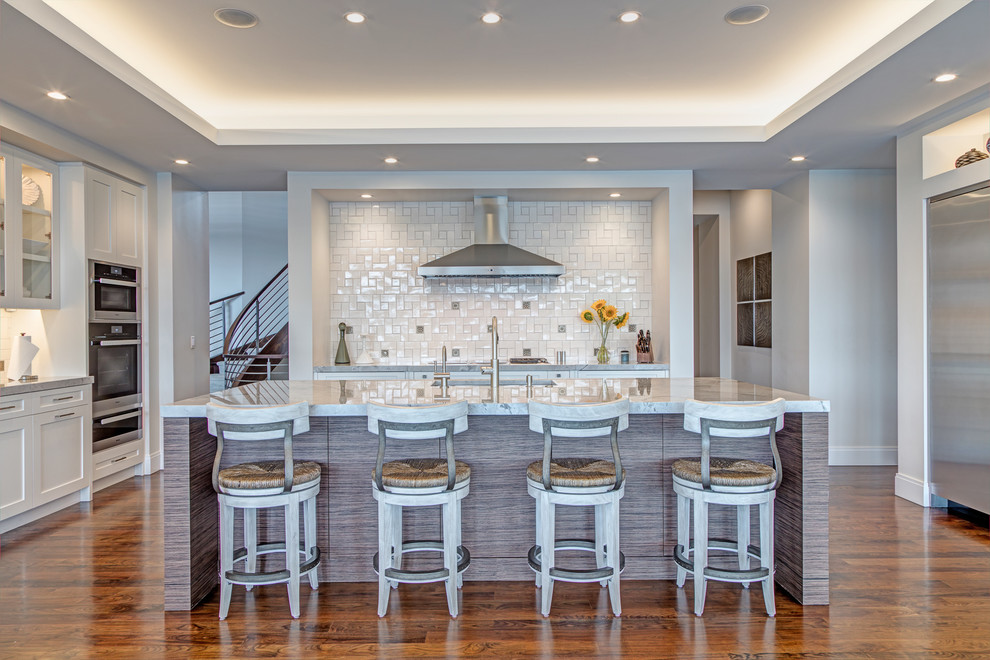 Mid-sized transitional single-wall open plan kitchen in Detroit with an undermount sink, shaker cabinets, white cabinets, white splashback, stainless steel appliances, medium hardwood floors, with island, brown floor, granite benchtops, porcelain splashback and white benchtop.