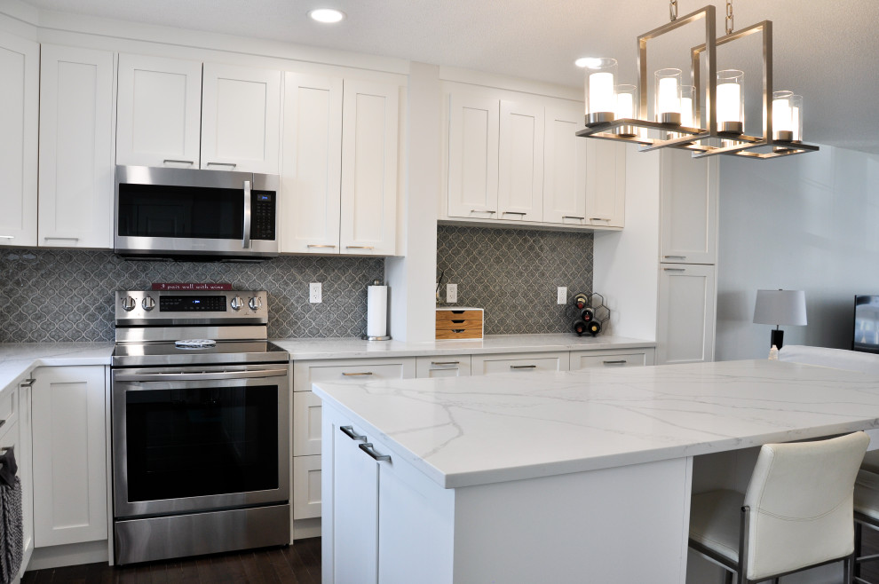 This is an example of a medium sized contemporary l-shaped kitchen/diner in Calgary with a submerged sink, shaker cabinets, white cabinets, engineered stone countertops, grey splashback, ceramic splashback, stainless steel appliances, an island and white worktops.