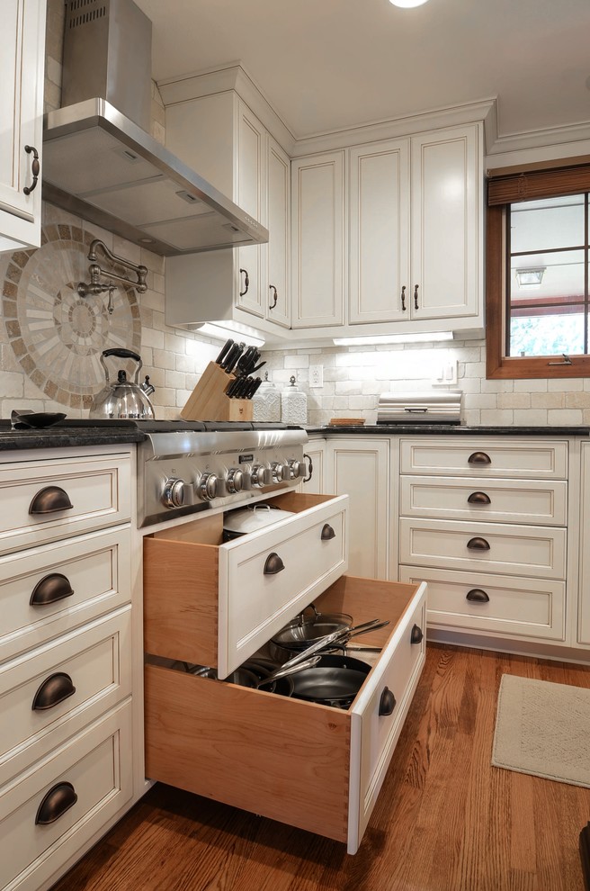 Eat-in kitchen - large transitional galley medium tone wood floor eat-in kitchen idea in Denver with an undermount sink, white cabinets, granite countertops, beige backsplash, stone tile backsplash, stainless steel appliances and an island