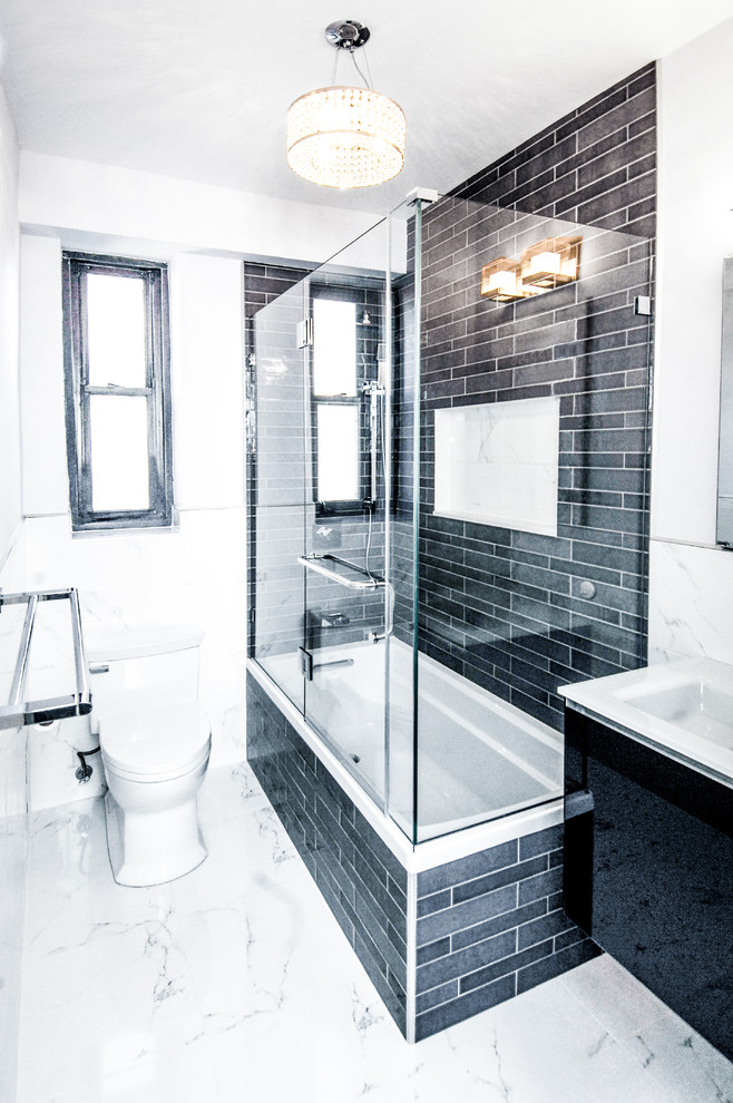 This is an example of a mid-sized transitional 3/4 bathroom in New York with flat-panel cabinets, black cabinets, an alcove tub, a shower/bathtub combo, a one-piece toilet, black tile, slate, white walls, marble floors, an integrated sink, white floor and a hinged shower door.