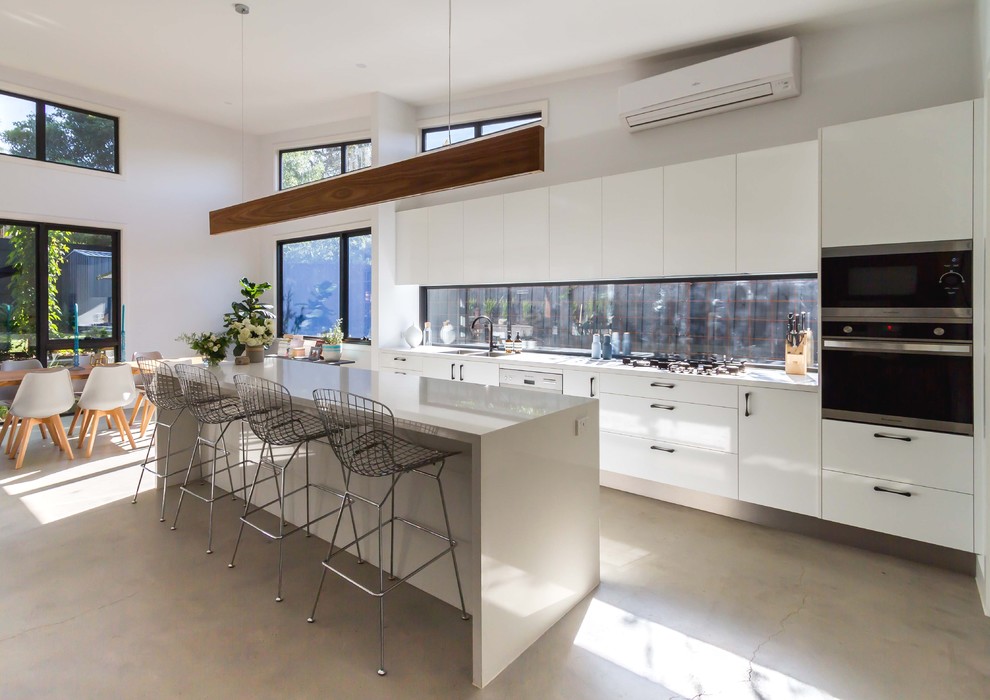 Large contemporary galley open plan kitchen in Melbourne with a double-bowl sink, flat-panel cabinets, white cabinets, quartz benchtops, window splashback, stainless steel appliances, concrete floors and with island.