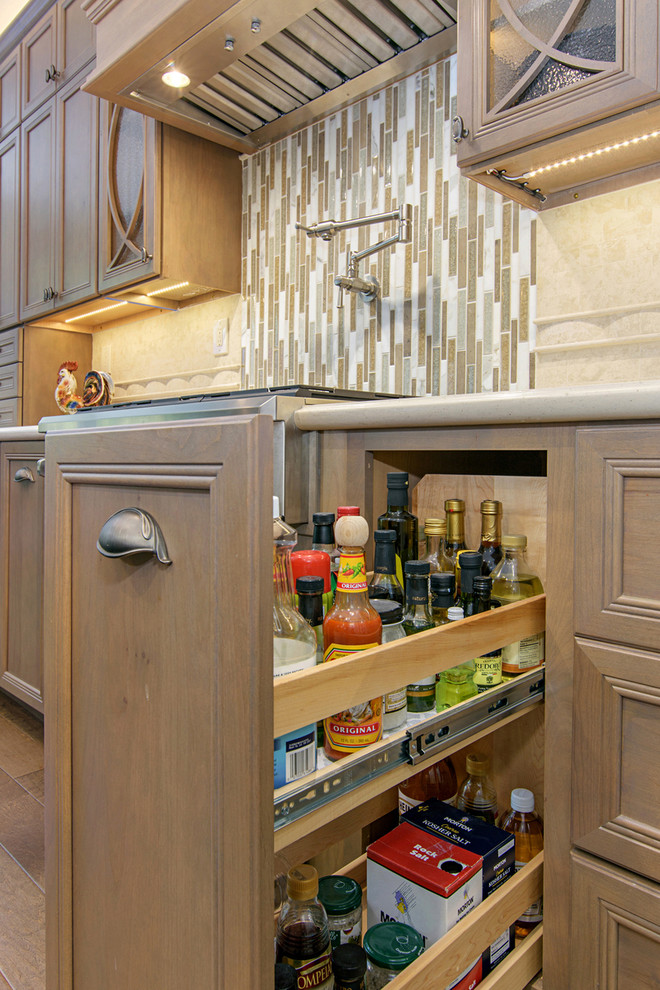 Example of a large transitional l-shaped medium tone wood floor and brown floor open concept kitchen design in San Diego with recessed-panel cabinets, medium tone wood cabinets, quartz countertops, beige backsplash, travertine backsplash, paneled appliances and an island