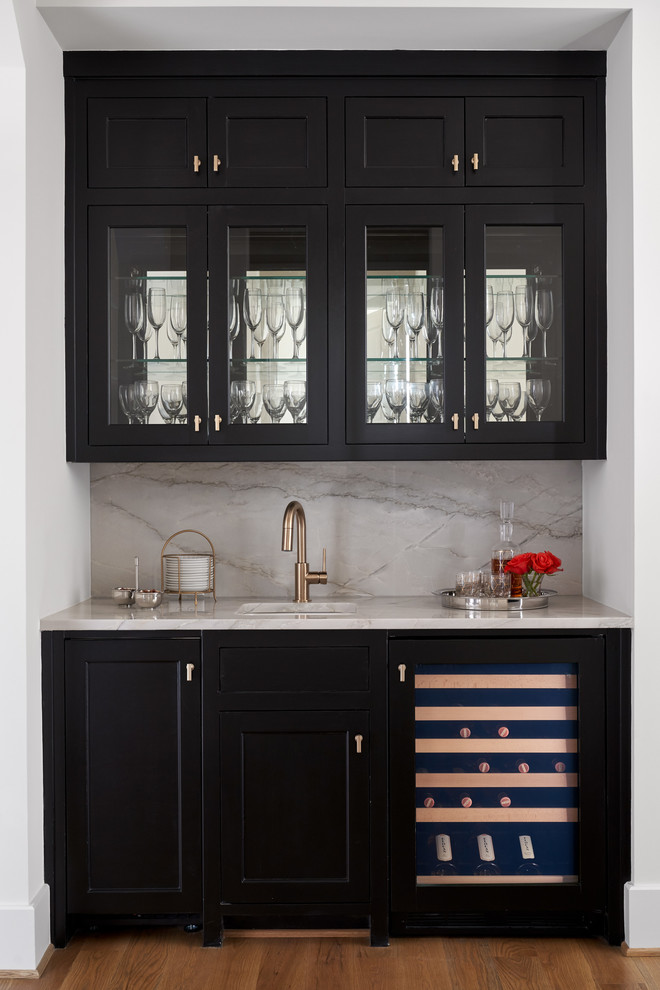 Small transitional single-wall wet bar in Dallas with an undermount sink, glass-front cabinets, black cabinets, white splashback, medium hardwood floors and beige floor.