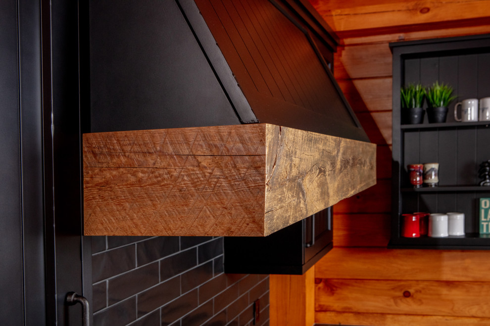Mid-sized mountain style l-shaped medium tone wood floor and brown floor eat-in kitchen photo with a farmhouse sink, shaker cabinets, black cabinets, quartz countertops, black backsplash, stainless steel appliances, an island and black countertops