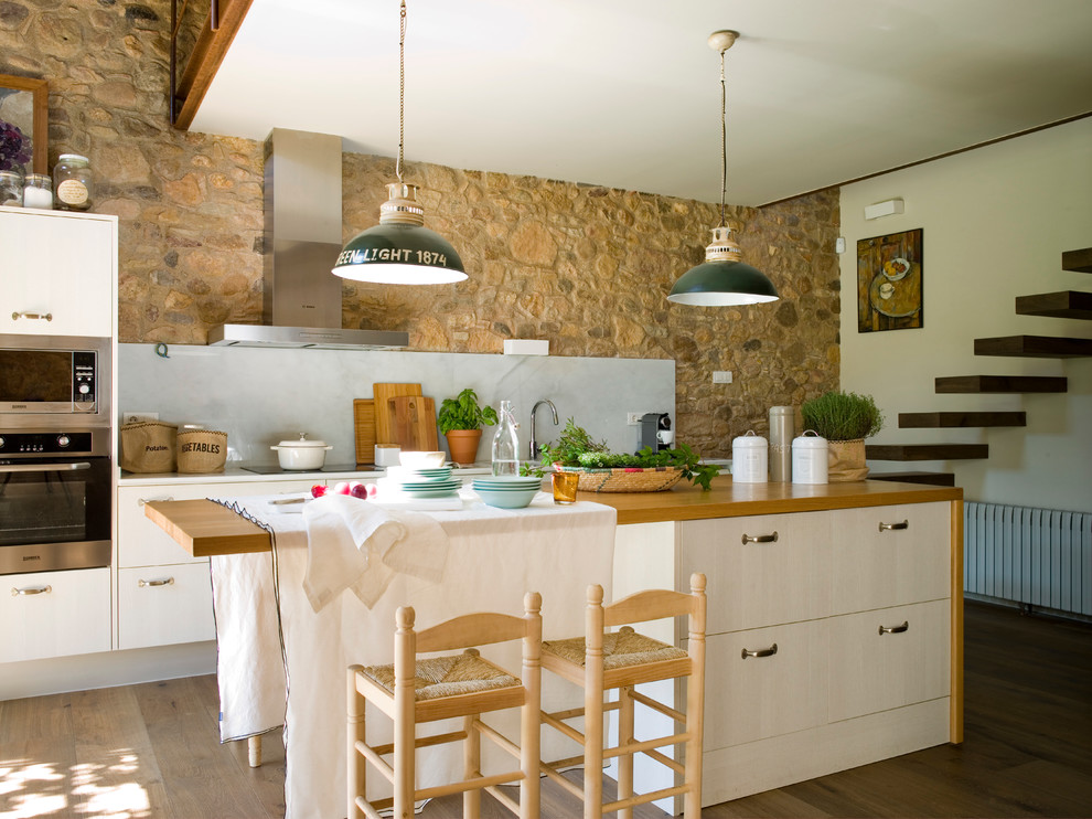 Inspiration for a large country galley separate kitchen in Barcelona with flat-panel cabinets, beige cabinets, wood benchtops, grey splashback, stone slab splashback, stainless steel appliances, medium hardwood floors and with island.