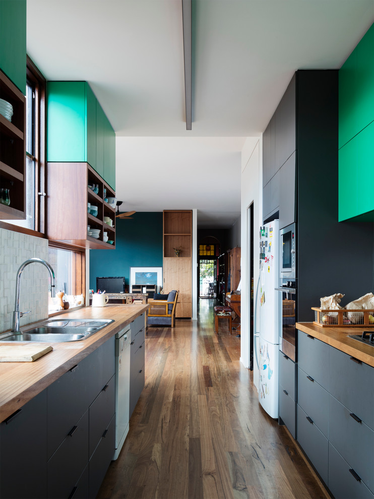 Photo of a mid-sized contemporary galley kitchen in Melbourne with a double-bowl sink, grey cabinets, wood benchtops, white splashback, ceramic splashback, white appliances, medium hardwood floors and no island.