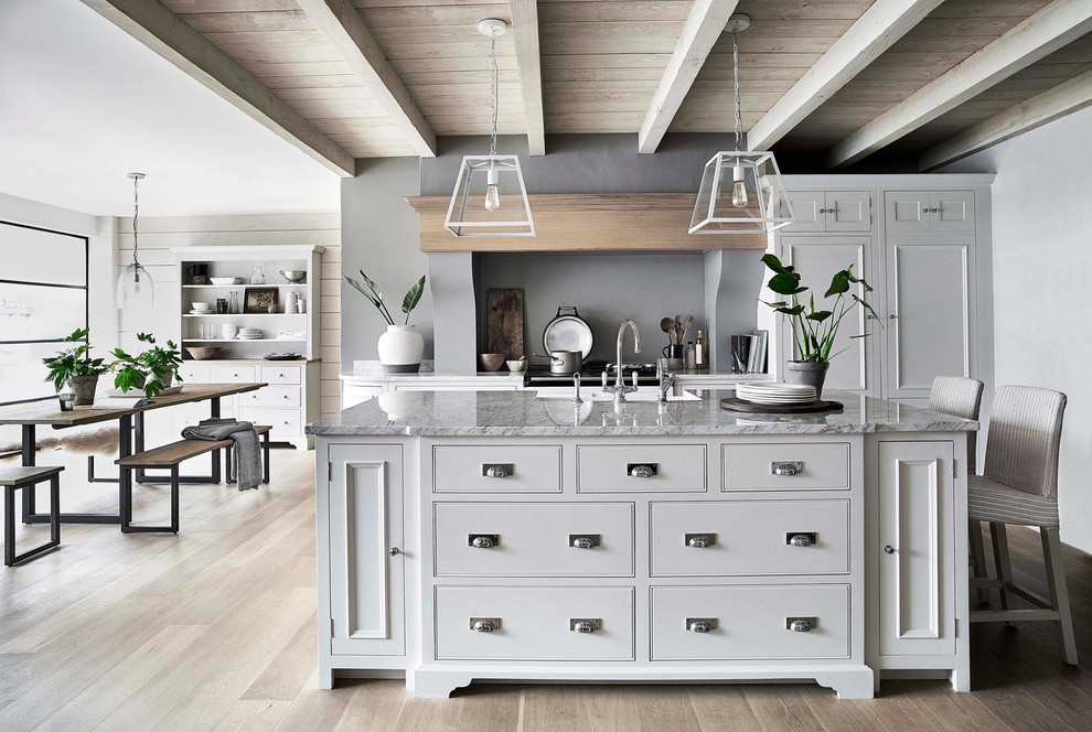 Inspiration for a large traditional galley eat-in kitchen in Other with white cabinets, with island, a farmhouse sink, beaded inset cabinets, marble benchtops, grey splashback, light hardwood floors and grey benchtop.