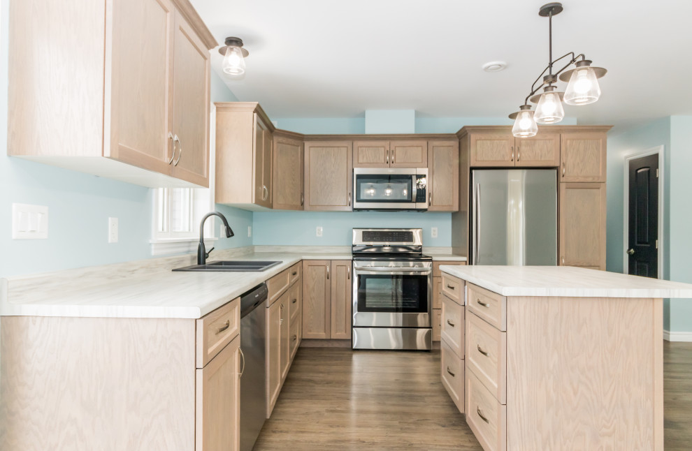 Mid-sized l-shaped laminate floor and brown floor kitchen photo with a double-bowl sink, recessed-panel cabinets, light wood cabinets, laminate countertops, stainless steel appliances, an island and white countertops