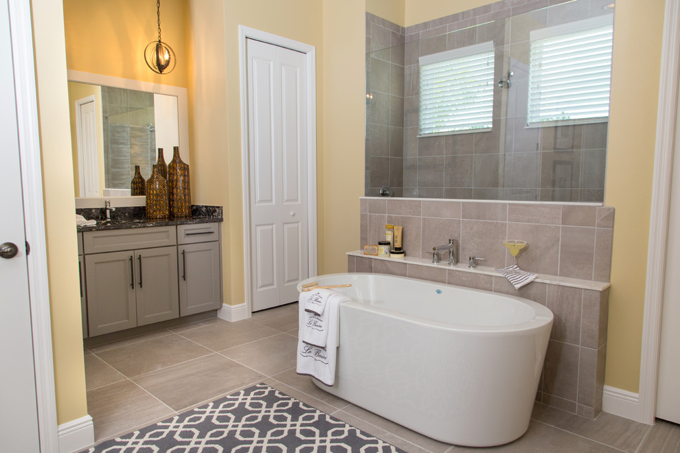 Transitional bathroom in Orlando with recessed-panel cabinets, grey cabinets, a freestanding tub, an alcove shower, gray tile and yellow walls.