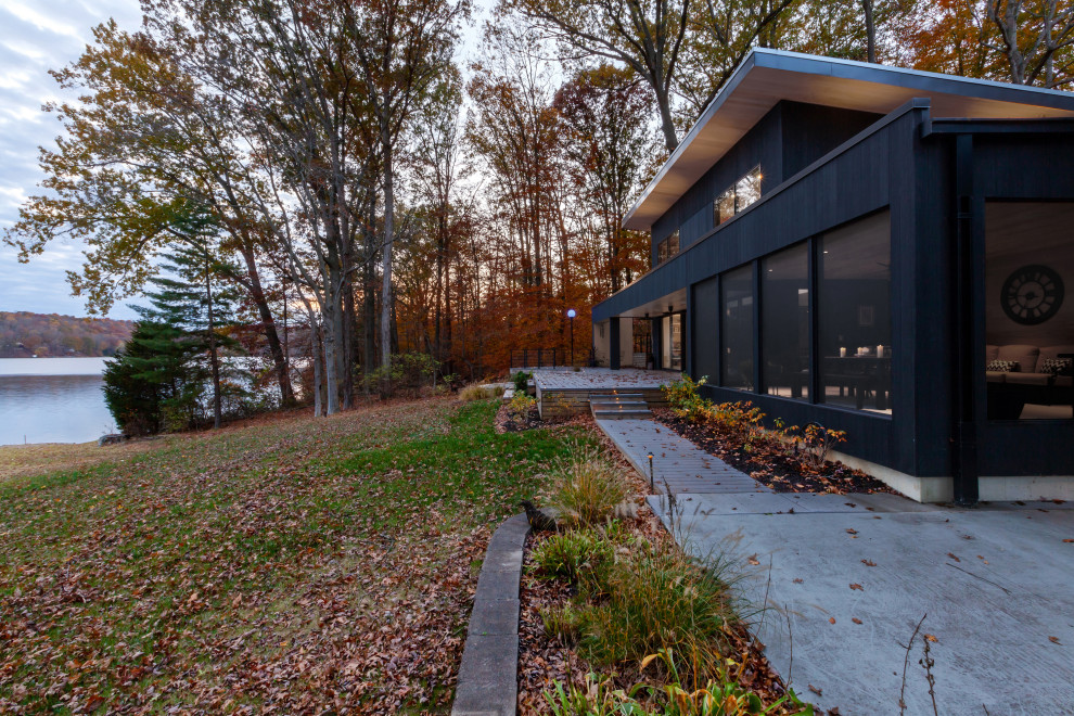 Inspiration pour une façade de maison noire minimaliste en bois de taille moyenne et à un étage avec un toit en appentis, un toit en métal et un toit gris.