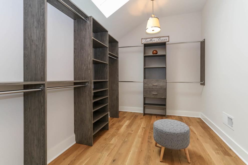 Large country gender-neutral walk-in wardrobe in Chicago with medium wood cabinets and light hardwood floors.
