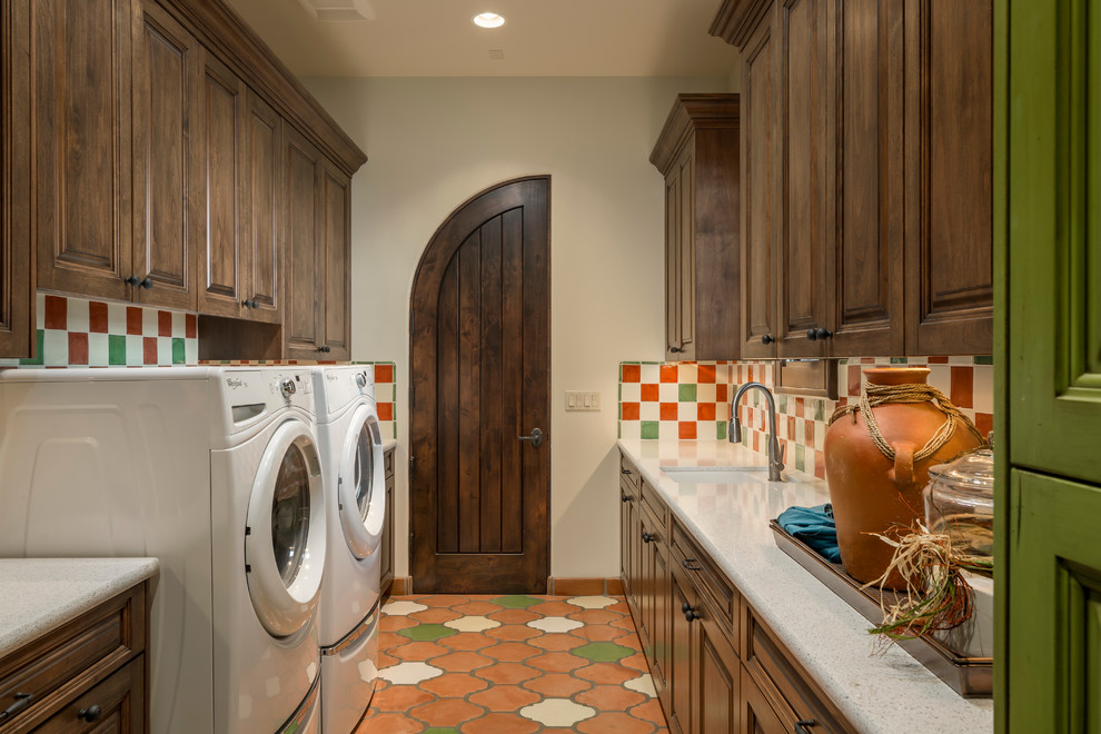 This is an example of a mediterranean galley dedicated laundry room in Phoenix with an undermount sink, raised-panel cabinets, dark wood cabinets, beige walls, terra-cotta floors, a side-by-side washer and dryer and white benchtop.