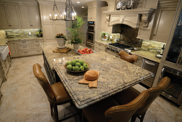 Inspiration for a large transitional ceramic tile kitchen remodel with a farmhouse sink, beige cabinets, granite countertops, stone tile backsplash, stainless steel appliances and an island
