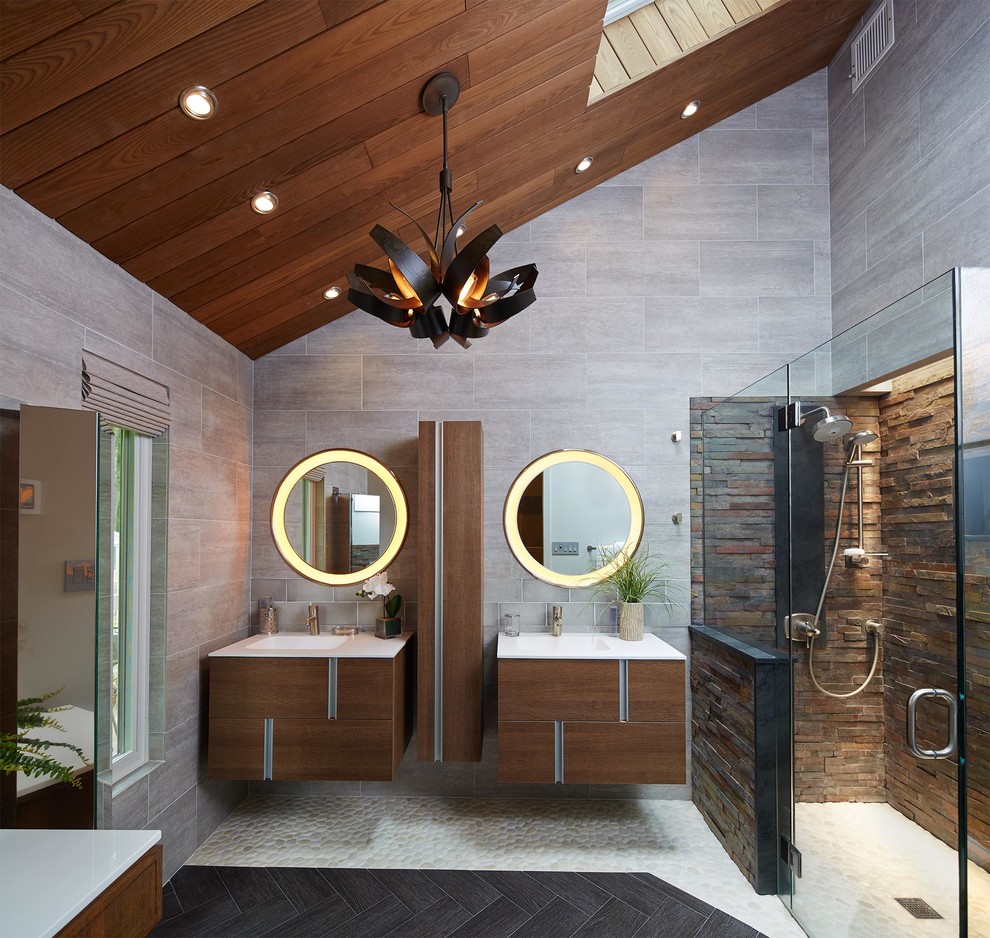 This is an example of a small contemporary master bathroom in New York with furniture-like cabinets, medium wood cabinets, solid surface benchtops, a curbless shower, a wall-mount toilet, black tile and pebble tile.