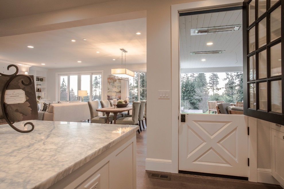 Inspiration for an expansive country l-shaped open plan kitchen in Seattle with a farmhouse sink, shaker cabinets, white cabinets, marble benchtops, white splashback, stone tile splashback, stainless steel appliances, dark hardwood floors and with island.