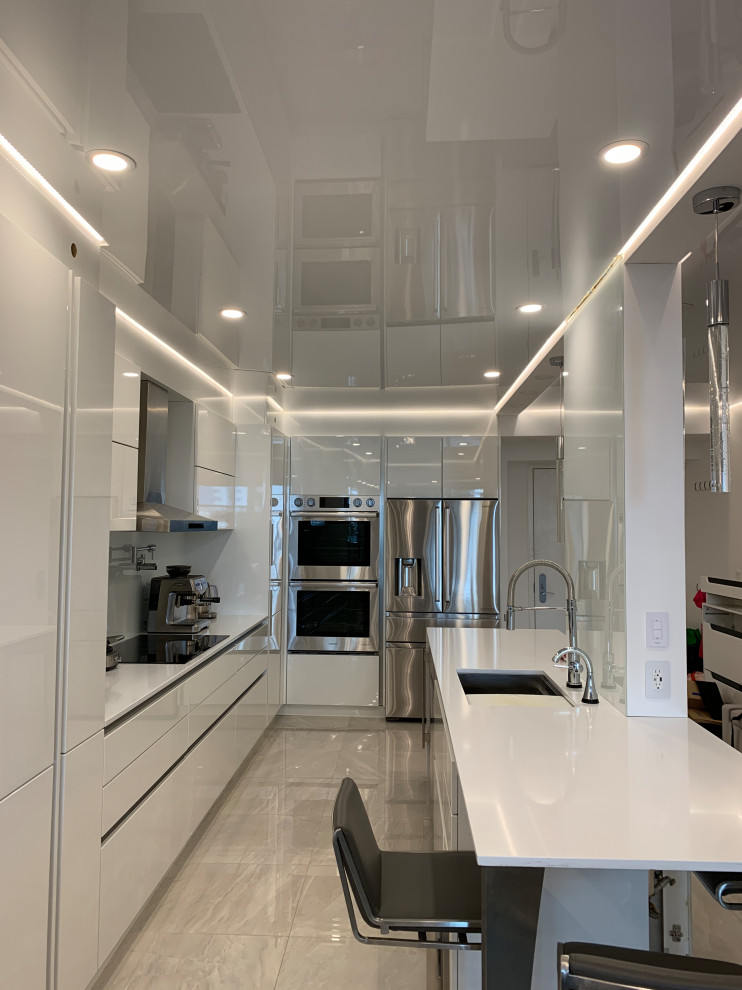 This is an example of a mid-sized galley eat-in kitchen in Miami with flat-panel cabinets, white cabinets, white splashback, porcelain floors, no island, grey floor, white benchtop and wallpaper.