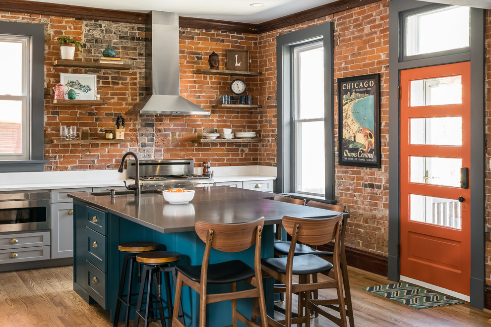 Mid-sized eclectic medium tone wood floor kitchen photo in St Louis with a single-bowl sink, shaker cabinets, gray cabinets, quartz countertops, brick backsplash, stainless steel appliances, an island and white countertops