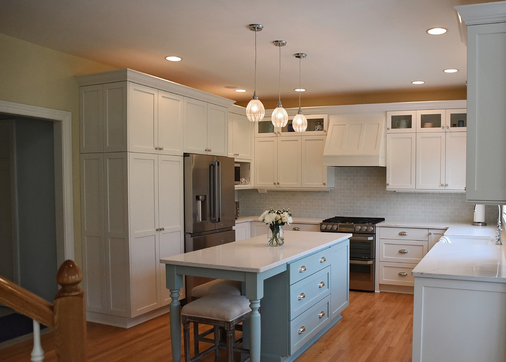 Example of a mid-sized transitional u-shaped medium tone wood floor and brown floor eat-in kitchen design with an undermount sink, flat-panel cabinets, white cabinets, quartz countertops, blue backsplash, ceramic backsplash, stainless steel appliances, an island and white countertops