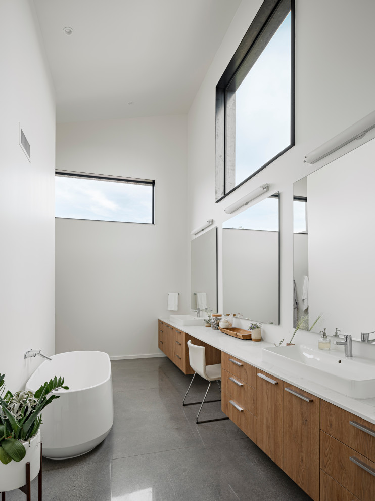 Bild på ett funkis vit vitt badrum, med släta luckor, skåp i mellenmörkt trä, ett fristående badkar, en dusch i en alkov, vit kakel, vita väggar, betonggolv, ett fristående handfat och bänkskiva i kvarts